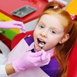 little girl smiling in red dental chair. The dentist examines the teeth of the child's patient.