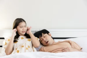 Woman covers ears as man snores beside her—showcasing the need for expert sleep apnoea care from Andrew Baderski Dental